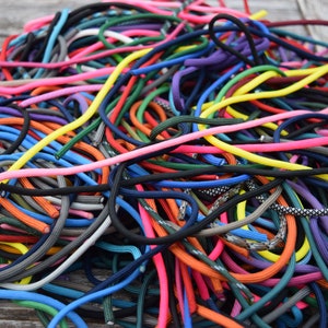 May include: A tangled pile of colorful shoelaces in various shades, including pink, yellow, blue, and black. The laces are made of a woven material and are of varying thicknesses. The image is a close-up shot, highlighting the texture and vibrant colors.