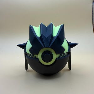 May include: A spherical object featuring a black and light yellow colour scheme. The top section has a jagged, crown-like structure with pointed protrusions on the sides. A circular yellow eye-like feature is centred above a row of sharp teeth.