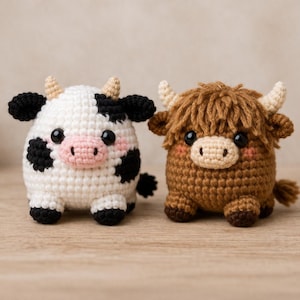 Puede incluir: Dos animales de peluche de ganchillo: una vaca blanca con manchas negras y una nariz rosa, y una vaca de las Highlands marrón con pelaje hirsuto. Ambos tienen ojos negros y cuernos pequeños. Los juguetes están hechos a mano.