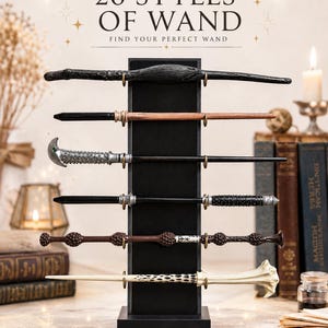 Op de afbeelding: Een zwarte verticale displaystandaard met zes verschillende toverstokken. De tekst bovenaan luidt 26 STYLES OF WAND FIND YOUR PERFECT WAND. De stokken variëren in kleur en textuur, met zwarte, bruine, zilveren en crèmekleurige afwerkingen.