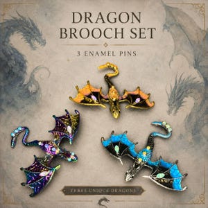 May include: A set of three dragon brooch enamel pins featuring intricate designs. One pin is gold with orange wings, one is iridescent purple with dark wings, and one is silver with bright blue wings. Each pin includes small embedded crystals.