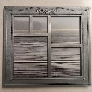 May include: A square, dark gray metal frame designed to resemble a window pane with multiple sections. The frame features a decorative scrollwork detail at the top center and a textured border. It contains a black and white landscape print.