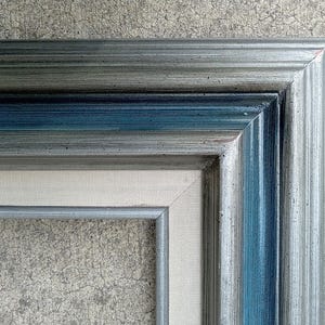 May include: A rectangular picture frame featuring a multi-layered design with a metallic silver outer edge, a deep blue inner band, and a light beige fabric-textured liner. The frame has a ridged, stepped profile with a visible corner miter joint.