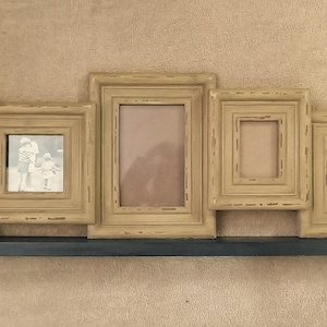 May include: A multi-frame wall decor piece with five beige-colored picture frames of varying sizes. The frames are mounted on a dark blue shelf. One frame contains a black and white photo. The frames have a distressed finish.