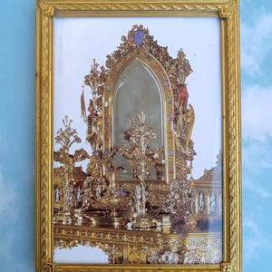 May include: A rectangular gold-toned frame containing a print of an ornate, metallic, gothic-style mirror structure. The central mirror is arched and surrounded by intricate, sculptural gold and silver metalwork featuring figures and floral motifs.