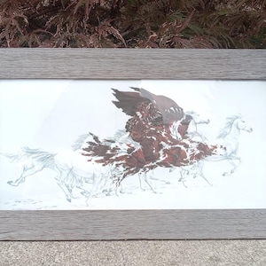May include: A rectangular framed print featuring a detailed illustration of a rider on horseback surrounded by several running horses. The artwork uses a palette of deep reddish-brown and white, set within a textured, weathered gray wooden frame.