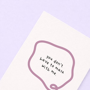 May include: A white card with the text "you don't have to mask with me" inside a mauve-colored, irregular-shaped border. The card is set against a light purple background.