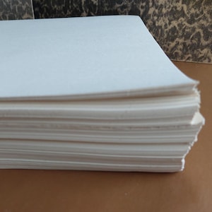 May include: A stack of rectangular white paper sheets with smooth edges, arranged in a neat pile. The paper is opaque and bright white, showing a clean, uniform surface texture across the top sheet and the layered edges of the entire stack.