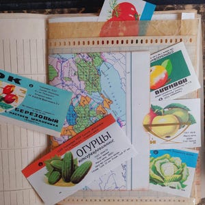 May include: An open book with vintage ephemera, including colorful labels with Cyrillic text and illustrations of fruits and vegetables. A map and other papers are also visible.