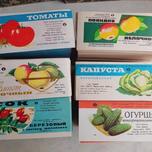 May include: A collection of vintage food product labels featuring illustrations of tomatoes, apples, cabbage, cucumbers, and rose hips. The labels have text in Russian and are in various colors, including blue, red, and green.
