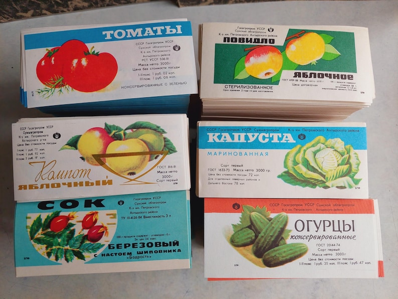 May include: A collection of vintage food product labels featuring illustrations of tomatoes, apples, cabbage, cucumbers, and rose hips. The labels have text in Russian and are in various colors, including blue, red, and green.