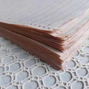 Peut inclure: Une pile de feuilles de papier blanc cassé vieilli avec un aspect taché de thé. Le papier présente de fines lignes verticales sombres et un bord perforé avec une rangée de petits trous circulaires. Les bords sont légèrement irréguliers.