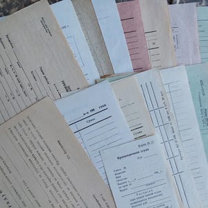 May include: A collection of vintage paper documents and forms in various shades of beige, white, pink, and light green. The papers feature printed black text in Cyrillic, including headings like Kраткосрочная ссуда, along with lines for data entry.