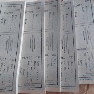 Könnte beinhalten: Fünf rechteckige graue Papiertickets mit schwarzem russischem Textaufdruck. Jedes Ticket enthält Felder für Reihe, Platz, Datum, Uhrzeit und Preis, mit dem Wort "контроль" am unteren Rand und individuellen Seriennummern wie 067701.