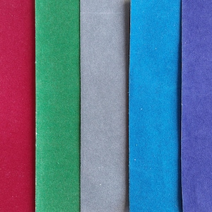 May include: Five vertical strips of fabric arranged side by side, featuring a smooth, matte texture. The colors from left to right are deep red, vibrant green, neutral gray, bright blue, and a rich purple, all displayed in a flat, uniform layout.