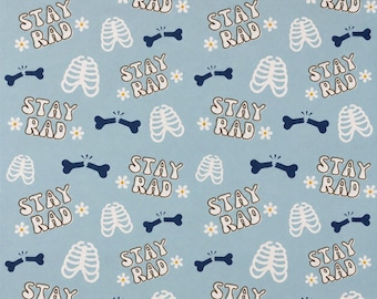 May include: Light blue fabric featuring a repeating pattern of white rib cages, dark blue broken bones, small white flowers, and the text STAY RAD in a brown outlined font. A wooden ruler is visible at the bottom, measuring up to 30 cm.