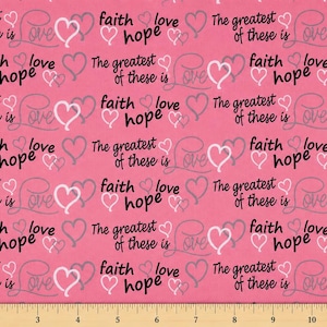 Könnte beinhalten: Ein rosa Stoff mit einem sich wiederholenden Muster aus schwarzem Text mit den Wörtern faith, love, hope und The greatest of these is love, durchsetzt mit weißen und grauen Herzumrissen. Ein Lineal unten zeigt eine Skala von 30 cm.