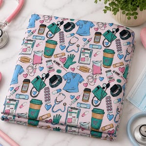 Puede incluir: Tela doblada con fondo rosa, con un estampado de ilustraciones médicas. El diseño incluye batas, estetoscopios, tazas de café y equipos médicos en verde azulado, azul y rosa. Se ve un estetoscopio y otros accesorios médicos.
