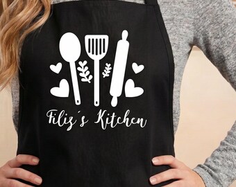 May include: A black apron featuring a white graphic print of a spoon, a spatula, a rolling pin, and several hearts. The text "Filiz's Kitchen" is printed in white script below the kitchen utensils. The code "M-01" is visible in the top left corner.