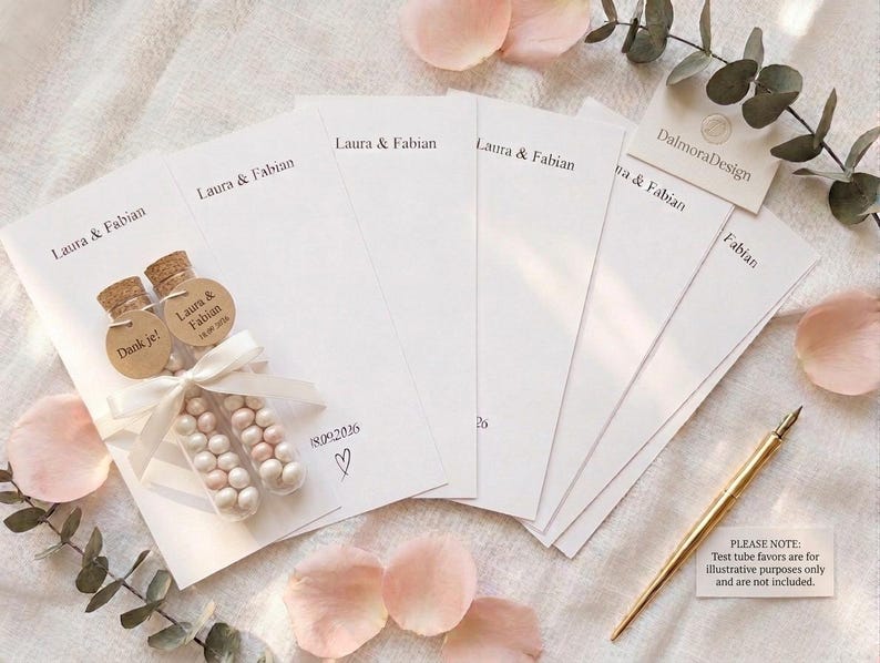Puede incluir: Un conjunto de tarjetas de papel rectangulares blancas impresas con los nombres Laura & Fabian y la fecha 18.09.2026 con un icono de coraz&oacute;n. Dos tubos de ensayo de vidrio rellenos de peque&ntilde;os caramelos blancos y rosas, corchos y cinta blanca.