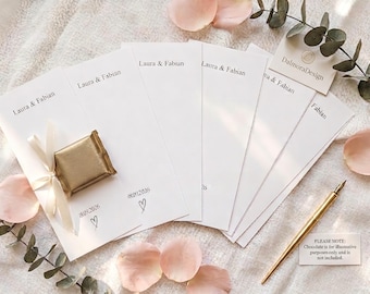 May include: A set of white rectangular paper cards printed with the names Laura & Fabian and the date 18.09.2026 with a heart icon. One card features a gold-wrapped square chocolate tied with a white ribbon. A gold pen and a small note are included.