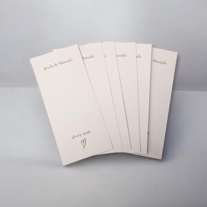 Puede incluir: Un conjunto de tarjetas de papel rectangulares de color blanco roto dispuestas en abanico. Cada tarjeta presenta el texto impreso "Şeyda & Mustafa" en la parte superior y la fecha "28-03-2026" seguida de un peque&ntilde;o coraz&oacute;n dibujado a mano.