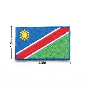 May include: Embroidered patch of the Namibian flag, measuring 6.35 cm wide and 3.81 cm tall. The design features a blue upper-left corner with a yellow sun, a red diagonal stripe, and a green lower-right corner.