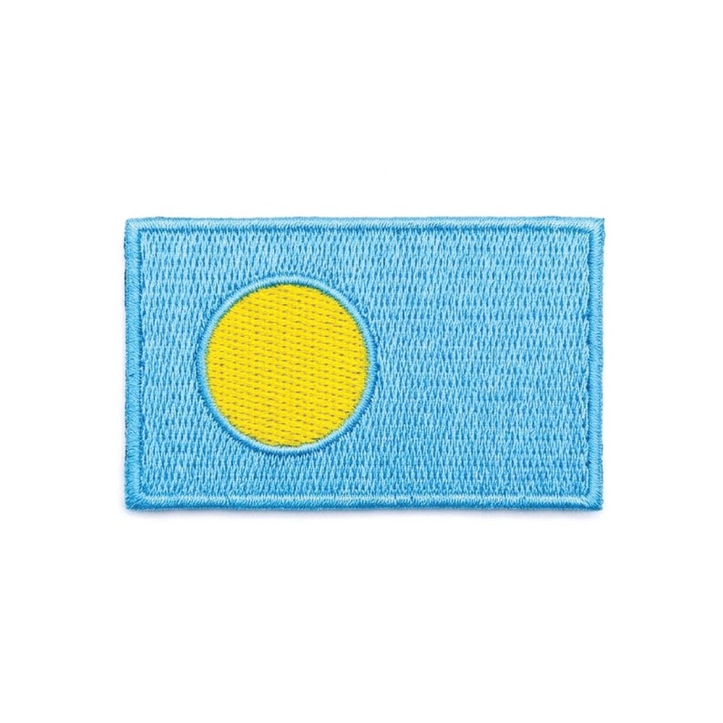 May include: Embroidered patch featuring the flag of Palau. The rectangular patch has a light blue background with a yellow circle in the center, offset towards the hoist side. The patch is bordered with a light blue stitching.