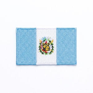 May include: Embroidered patch featuring the flag of Guatemala. The rectangular patch has light blue vertical stripes on either side of a white stripe. The Guatemalan coat of arms is centered on the white stripe.