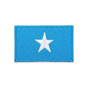 May include: Embroidered patch depicting the flag of Somalia. The patch has a light blue background with a white, five-pointed star in the centre. The edges are neatly stitched with a blue border.