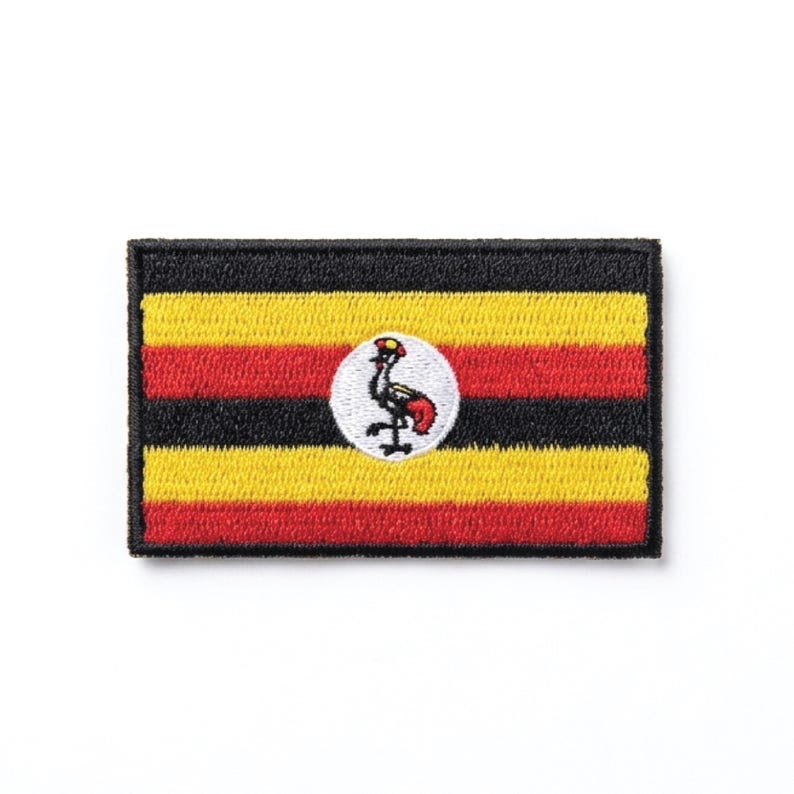 Op de afbeelding: Geborduurde patch met de vlag van Oeganda. De rechthoekige patch heeft horizontale strepen in zwart, geel en rood. Een witte cirkel in het midden toont een grijze kraanvogel met rode accenten. De patch heeft een zwarte rand.