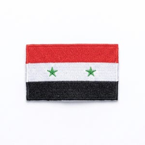 May include: Rectangular patch depicting the Syrian flag. The top section is red, the middle is white with two green stars, and the bottom is black. The patch is probably made of fabric and designed to be sewn or ironed on.