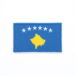 May include: A rectangular patch featuring the flag of Kosovo. The flag has a blue background with six white stars above a yellow map of Kosovo. The patch is bordered with blue stitching.