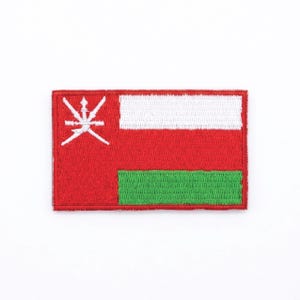 Pode incluir: Patch bordado com a bandeira de Omã. O patch retangular tem um fundo vermelho com uma faixa branca na parte superior e uma faixa verde na parte inferior. Um emblema branco está à esquerda.