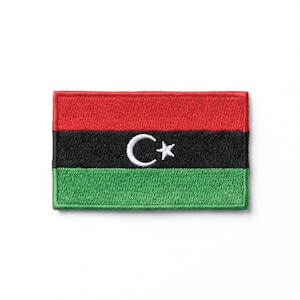 May include: Embroidered patch depicting the flag of Libya. The rectangular patch has horizontal stripes of red, black, and green. A white crescent moon and star are centered on the black stripe.