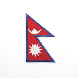 Pode incluir: Patch bordado com a bandeira do Nepal. A bandeira tem um formato único, com fundo vermelho e borda azul. Exibe uma lua crescente branca e um emblema solar.