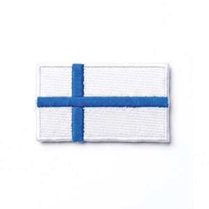 May include: A rectangular white patch featuring a blue Nordic cross. The cross is centrally positioned and has a bold, solid design. The patch is bordered in white and is likely an embroidered emblem.