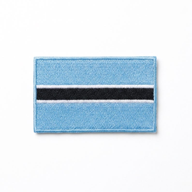 May include: A rectangular patch featuring the flag of Botswana. The flag has a light blue background with a horizontal black stripe in the center, edged with white. The patch is embroidered with a textured appearance.