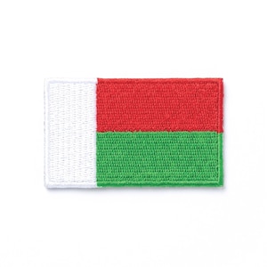 Puede incluir: Parche bordado con la bandera de Madagascar. El parche rectangular tiene una franja vertical blanca a la izquierda, con una franja horizontal roja sobre una franja horizontal verde a la derecha. El parche está sobre un fondo blanco.