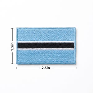 May include: A rectangular patch featuring the flag of Botswana. The patch is light blue with a black stripe in the center, bordered by a white stripe. The patch measures 2.5 inches wide and 1.5 inches high.
