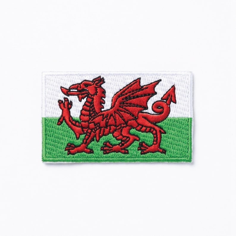 May include: Embroidered patch of the Welsh flag. It features a red dragon on a white and green background. The patch is rectangular with a stitched border.