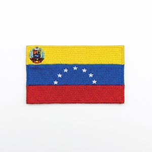 Könnte beinhalten: Gestickter Aufnäher mit der Flagge von Venezuela. Der rechteckige Aufnäher hat horizontale Streifen in Gelb, Blau und Rot, mit sieben weißen Sternen im blauen Streifen. Ein Wappen befindet sich in der oberen linken Ecke.