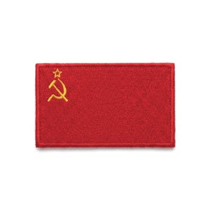 May include: A rectangular red patch featuring a gold hammer and sickle emblem with a gold star above it. The patch has a red border and is set against a white background.