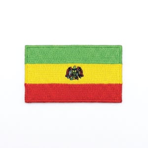 May include: Embroidered patch featuring the flag of Bolivia. The rectangular patch has horizontal stripes of green, yellow, and red. A detailed emblem is centered on the yellow stripe. The patch is likely for clothing or accessories.