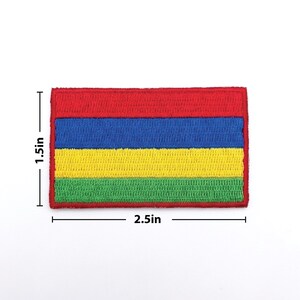 May include: A rectangular embroidered patch featuring horizontal stripes of red, blue, yellow, and green. The patch measures 2.5 inches wide and 1.5 inches high. The edges are neatly finished with a red border. This patch is suitable for clothing or accessories.