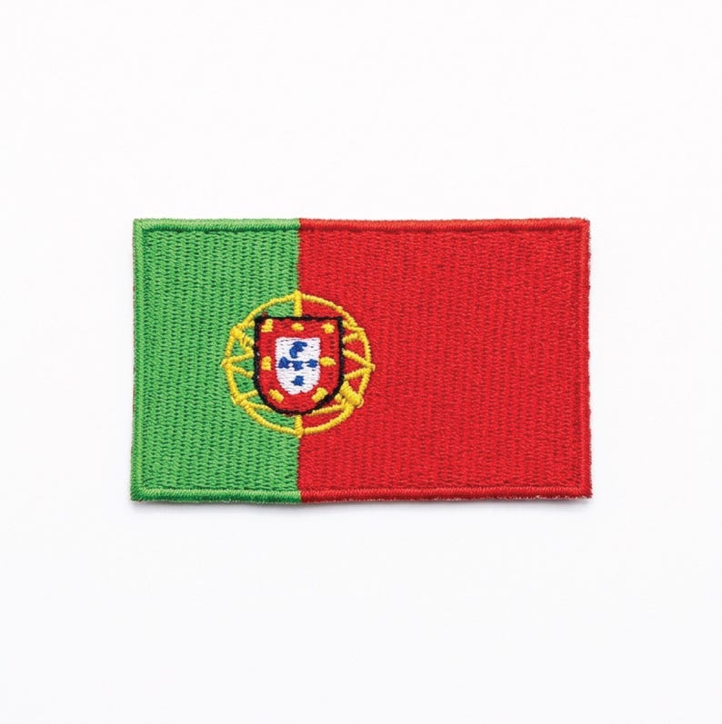 May include: Embroidered patch featuring the flag of Portugal. The design is divided vertically, with a green field on the left and a red field on the right. The Portuguese coat of arms is centered on the red field.