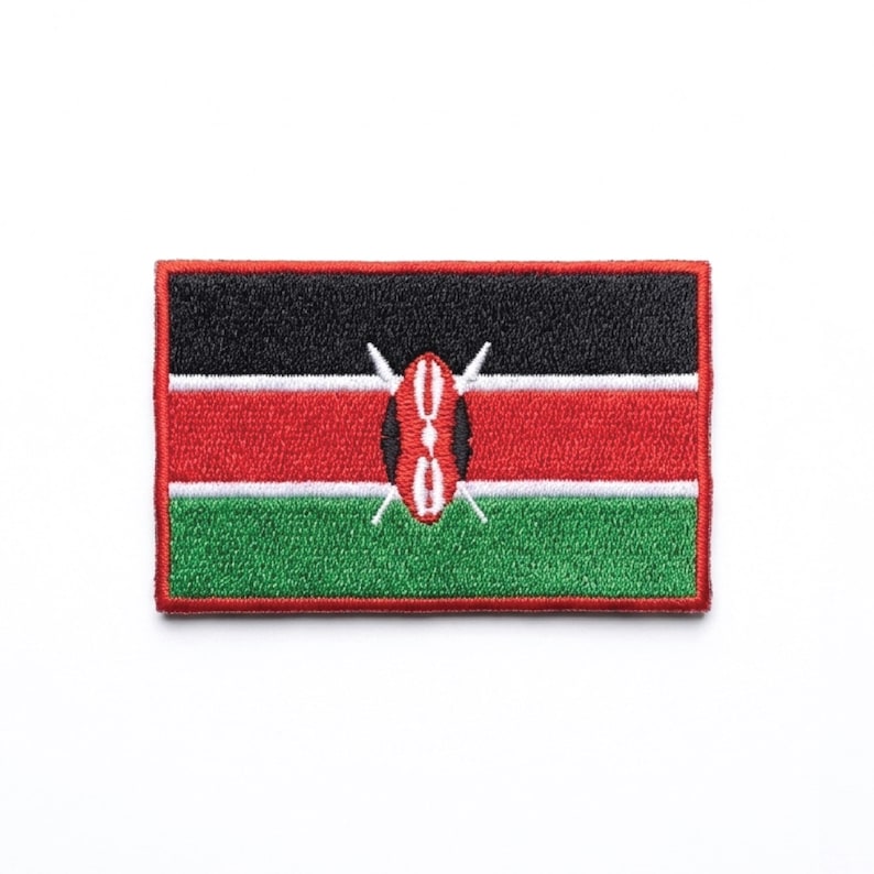 May include: Embroidered patch featuring the flag of Kenya. The rectangular patch has a black top stripe, a red middle stripe, and a green bottom stripe. A shield and spears are in the center. The patch is outlined in red.