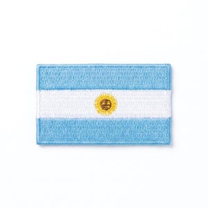 May include: Embroidered patch featuring the flag of Argentina. The design includes a light blue background with a white horizontal stripe in the center. A golden sun is centered on the white stripe. The patch has a rectangular shape.