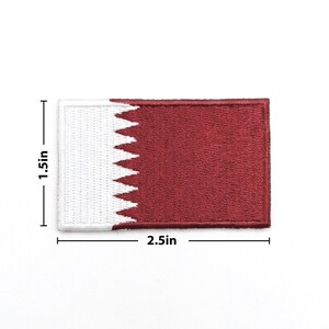 May include: A rectangular patch featuring the flag of Qatar. The patch is 2.5 inches long and 1.5 inches high. The flag design includes a white serrated band on the left and a maroon field on the right.