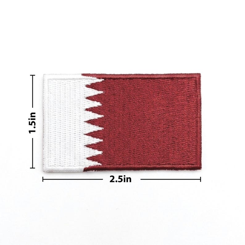 May include: A rectangular patch featuring the flag of Qatar. The patch is 2.5 inches long and 1.5 inches high. The flag design includes a white serrated band on the left and a maroon field on the right.